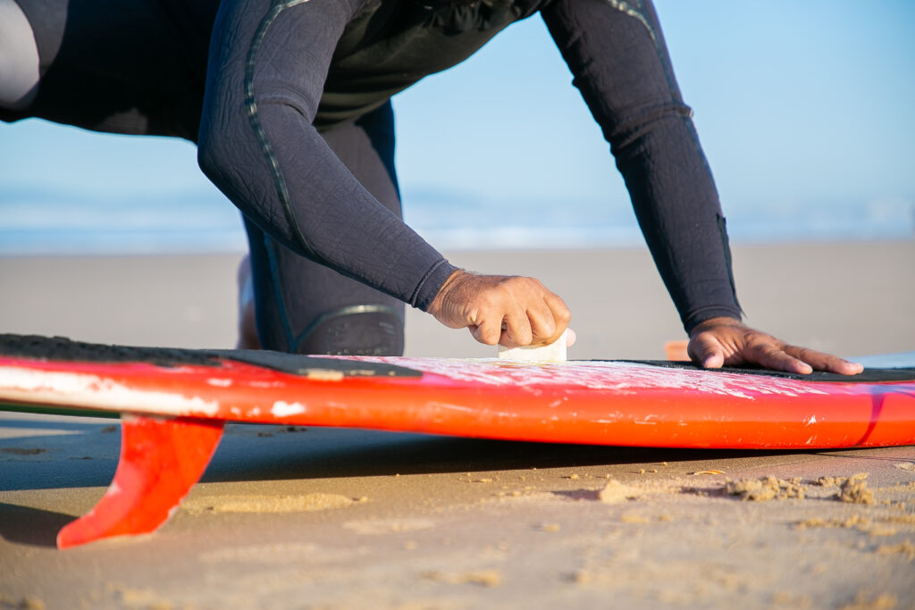 surf and camp. male surfer in wetsuit waxing his board on the beach